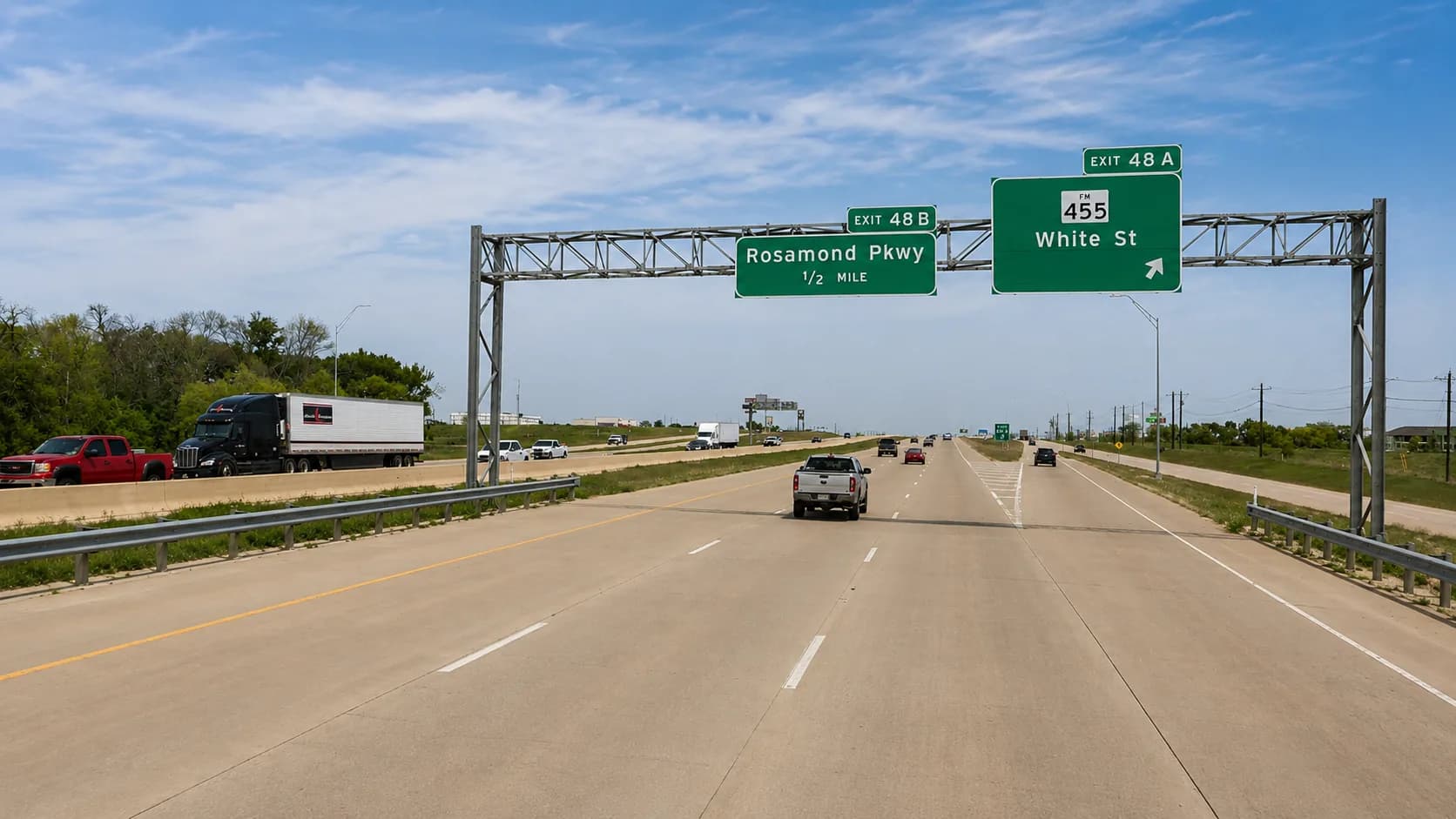 U.S. Highway 75 northbound through Anna, Texas, with an 18-wheeler and passenger vehicles approaching the Exit 48A (FM 455 / White Street) and Exit 48B (Rosamond Parkway) interchanges under a bright Texas sky
