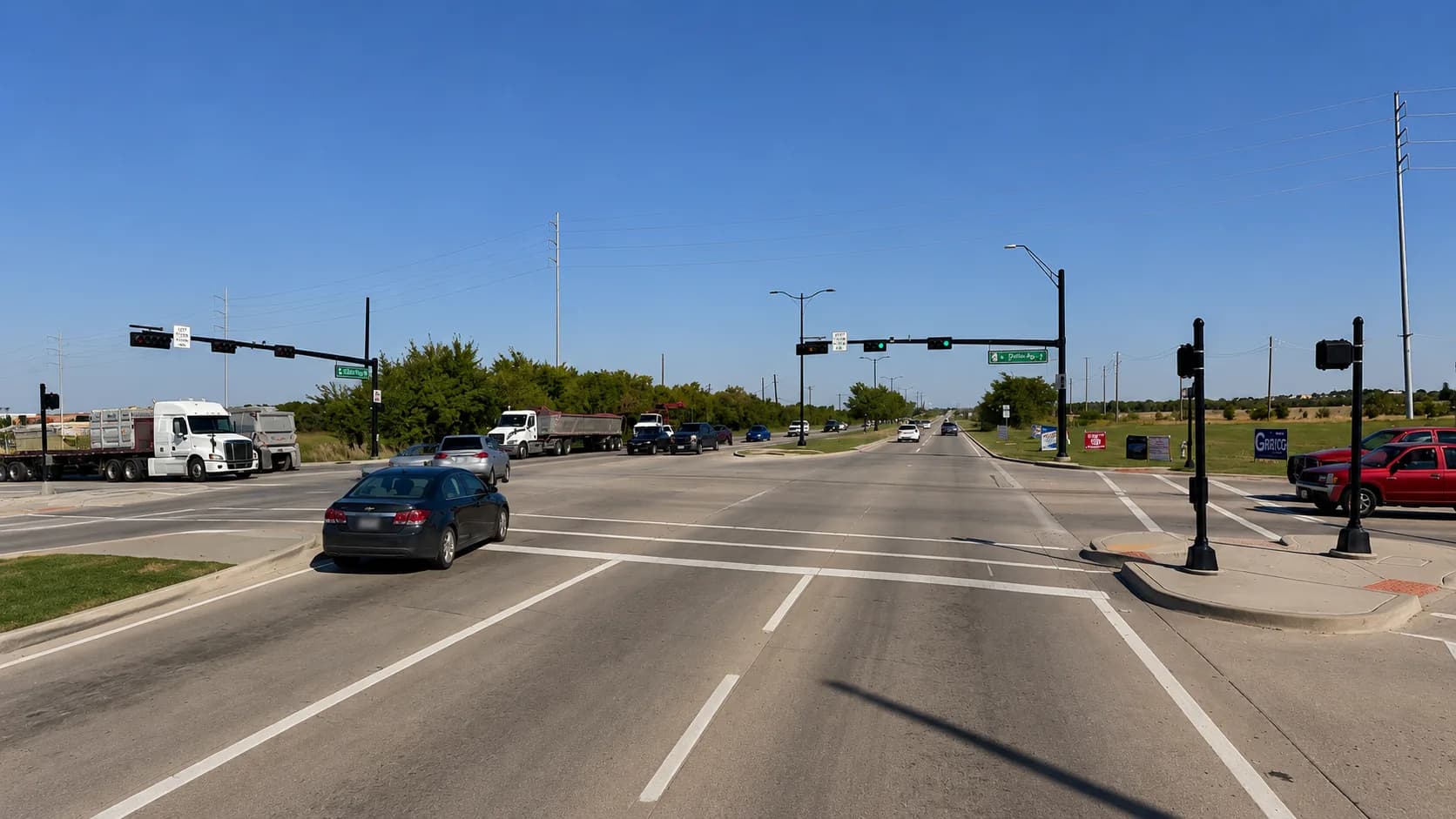 An 18-wheeler and dump trucks crossing a major Preston Road / State Highway 289 intersection in Celina, Texas, alongside passenger vehicles, with traffic signals controlling the busy commercial corridor under a bright Texas sky