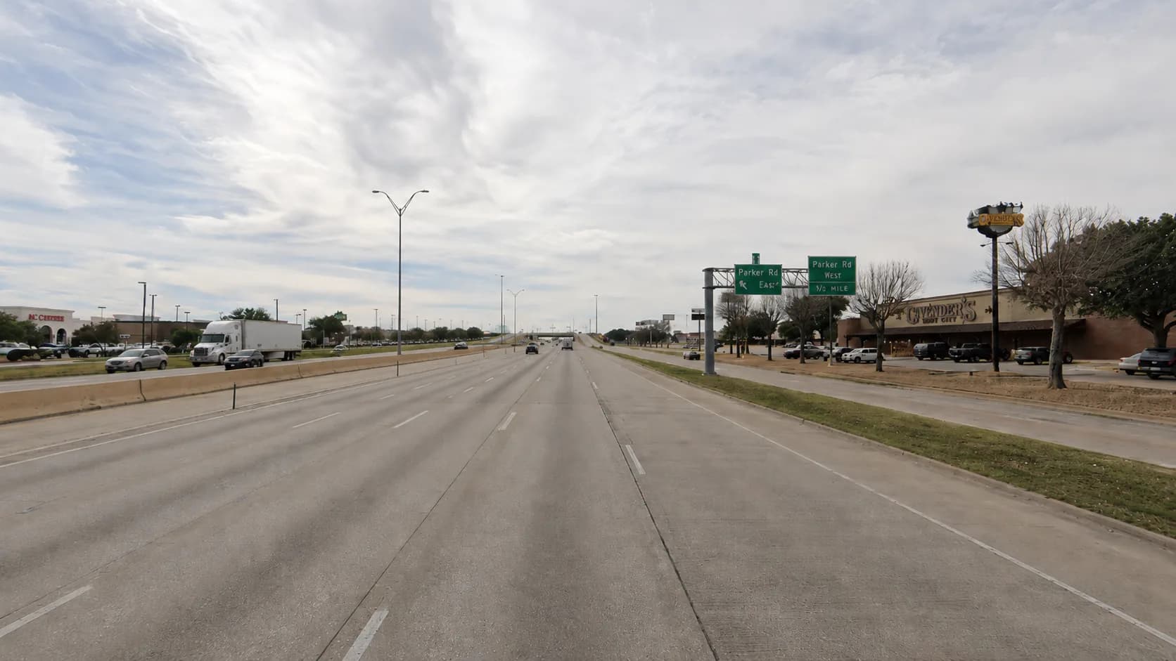 U.S. Highway 75, the Central Expressway, through Plano, Texas, with a commercial truck and passenger vehicles on the multilane corridor beneath overhead highway signage under an overcast Texas sky