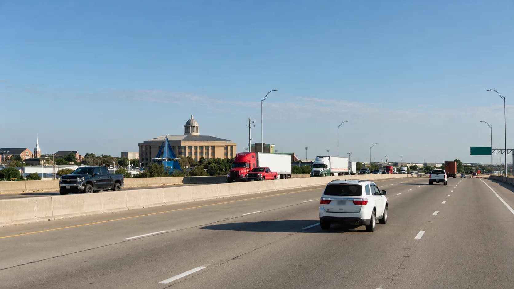 Interstate 30 through Rockwall, Texas, with an 18-wheeler and passenger vehicles passing the Rockwall County Courthouse dome under a clear Texas sky