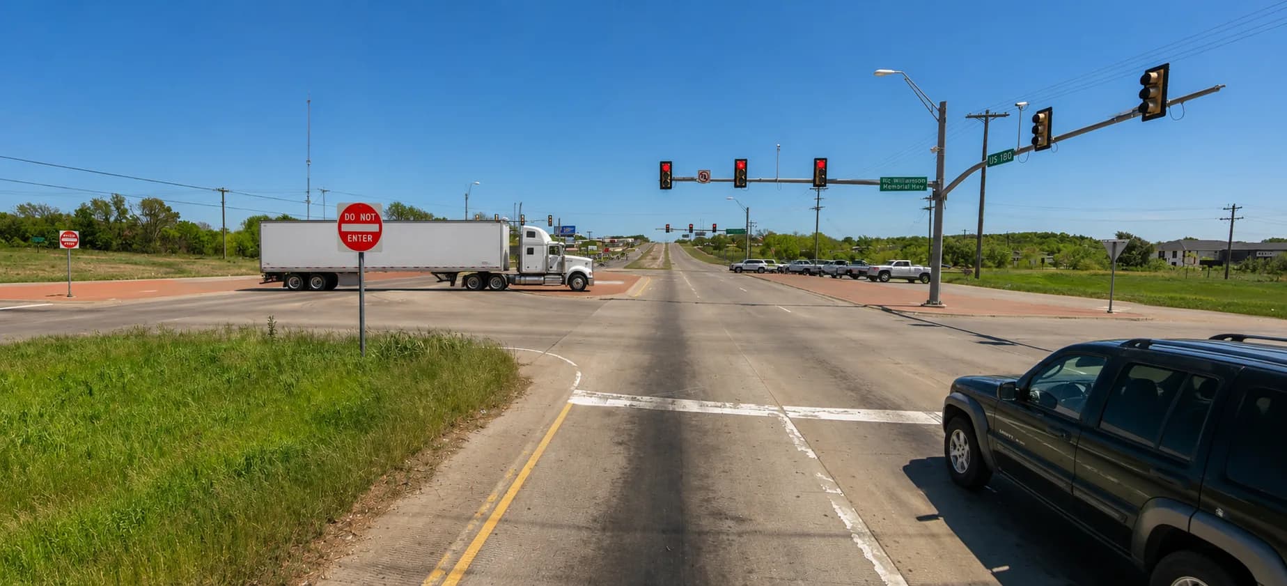 U.S. Highway 180 at Ric Williamson Memorial Highway in Weatherford, Texas, with an 18-wheeler turning through the signalized intersection under a bright Texas sky